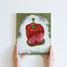 Load image into Gallery viewer, Two hands holding an oil painting of a bright, four lobed red pepper from the bottom. The pepper is vibrant and takes up most of the canvas, with a tall green stem. The pepper is surrounded by strokes of white paint, on top of a sage green background.
