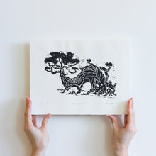 Load image into Gallery viewer, Two hands holding a small, black and white linocut print of a twisted and entangled tree. The tree slopes to the left and appears to be lively and moving. The print takes up a majority of the paper. It is numbered, titled, and signed underneath the print.

