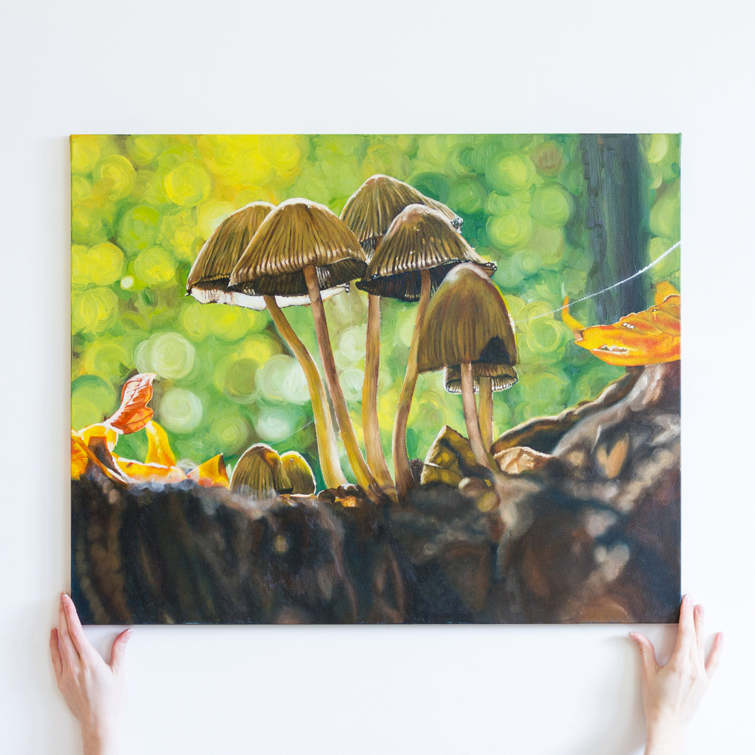 Two hands holding a large oil painting of five brown mushrooms on a bright green background. The mushrooms fill up most of the canvas. They are surrounded on the bottom by dirt and autumn leaves. The background is circles of blurry bright green.