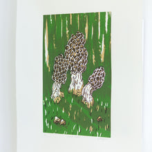 Load image into Gallery viewer, A side, angled view of a small screenprint of three morel mushrooms on a dark green background. The print is made up of three colours, an emerald green, a light brown, and a dark brown. The print is small on the paper, with large white borders around it.
