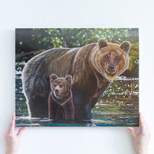 Load image into Gallery viewer, Two hands holding a large paper reproduction of a painting. The painting features two grizzly bears, a mother, and her young cub crossing a river. They are standing in shiny green and turquoise water, and there is a blurry green background behind them.
